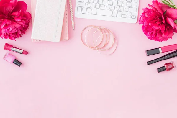 Flat lay blogger or freelancer workspace with a notebook, keyboard, red peonies on a pink background