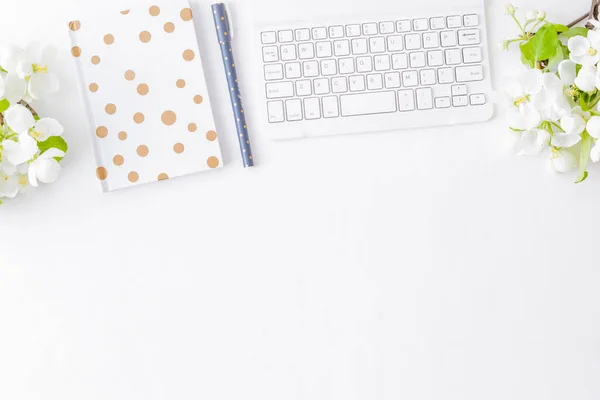 Flat lay blogger or freelancer workspace with a notebook, keyboard and white spring flowers on a white table