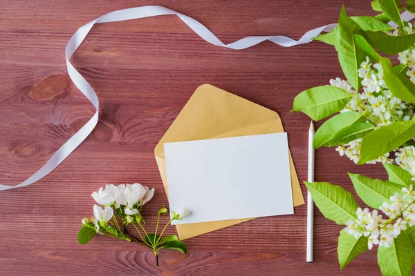 Mockup white greeting card and envelope with spring white flowers on a wooden background