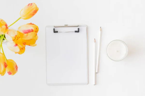 Flat lay blogger or freelancer workspace with a mockup clipboard and yellow tulips on a light background