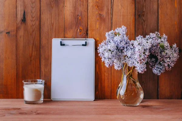 Mockup with a clipboard and branches of lilac in a vase on a wooden table