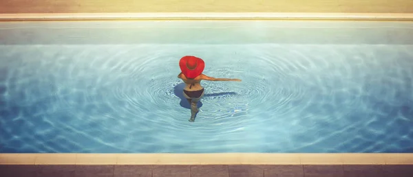 Jonge vrouw in een hoed in het zwembad bij zonsondergang — Stockfoto