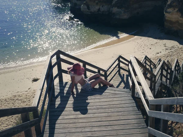 Hembra en un sombrero rojo en los escalones de madera de las escaleras en la playa de Portugal — Foto de Stock