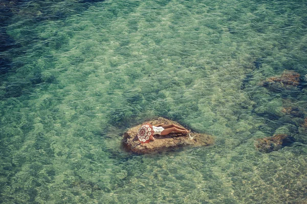 Mooi meisje op een rots in het midden van de zee met paraplu. Van bovenaf bekijken — Stockfoto