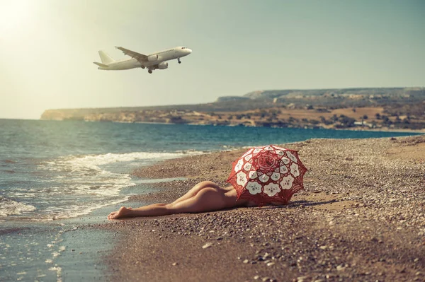 stock image Beautiful naked girl lying on the beach under an umbrella. Against the backdrop of the aircraft