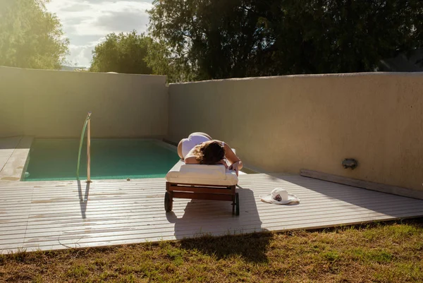 美丽的裸体女孩是躺在池边的躺椅上和日光浴在日落时分 — 图库照片