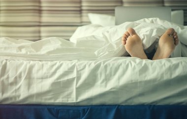 Kadın bacaklarını batımında battaniye altında. Görüntü'nün içinde laptop ile erkek