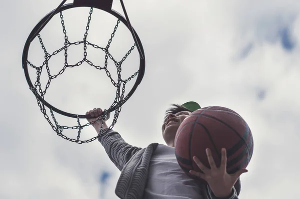 Un niño saltando y haciendo portería jugando streetball, baloncesto. Lanza una pelota de baloncesto al ring. El concepto de deporte —  Fotos de Stock