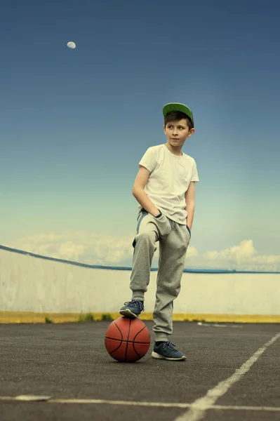 Un niño con una pelota de baloncesto en el fondo del cielo y la luna. El concepto de deporte —  Fotos de Stock