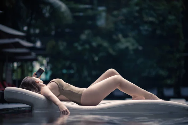 Piękna samotna dziewczyna leży na leżaku w strój kąpielowy w basenie w tropikach Malezji. Kobieta w wody w basenie — Zdjęcie stockowe