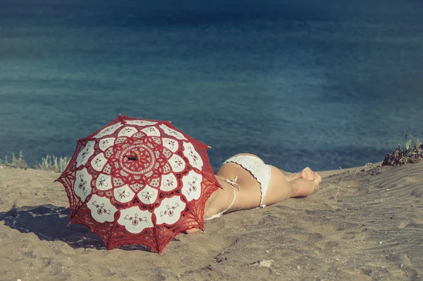 Bella femmina nuda si trova sulla spiaggia sotto un ombrellone rosso. Ragazza sulla sabbia sotto l'ombrello — Foto Stock