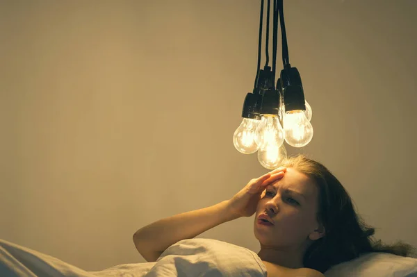 Ένα κορίτσι έγκειται στο κρεβάτι κάτω από μεγάλες λάμπες φωτός δεν μπορεί να κοιμηθεί. Έννοια εικόνα. Αϋπνία. Ψυχολογία. — Φωτογραφία Αρχείου