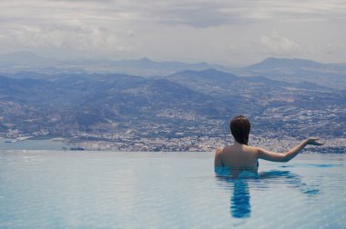 Volos Yunan şehir günbatımı ve dağlar, havuzun içinde belgili tanımlık geçmiş çatıda genç kadın. Çatıdaki yüzme havuzunda erkek