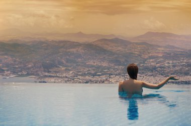Volos Yunan şehir günbatımı ve dağlar, havuzun içinde belgili tanımlık geçmiş çatıda genç kadın. Çatıdaki yüzme havuzunda erkek