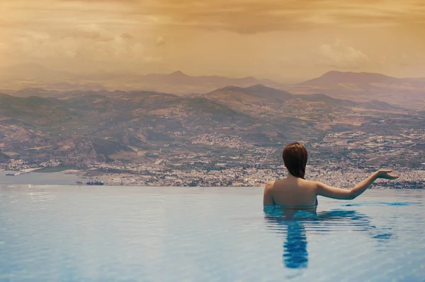 Jovem fêmea na piscina no telhado no fundo da cidade grega de Volos ao pôr-do-sol e montanhas. Feminino na piscina no telhado — Fotografia de Stock