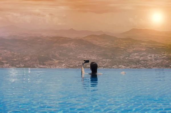 Jovem fêmea na piscina no telhado no fundo da cidade grega de Volos ao pôr-do-sol e montanhas. Feminino na piscina no telhado — Fotografia de Stock