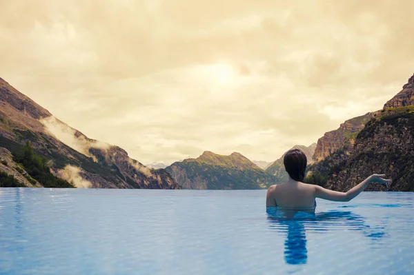 Jovem fêmea na piscina no telhado no fundo da Paisagem das Montanhas e nuvens do Tirol do Sul no pôr do sol — Fotografia de Stock