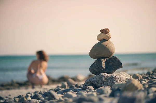 Belle femme en maillot de bain marchant le long de la plage sur fond de pyramide de pierres. Femme floue avec des pierres sur la plage — Photo