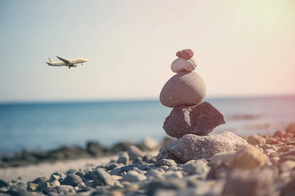 Pirâmide de pedras na praia contra o mar e avião . — Fotografia de Stock