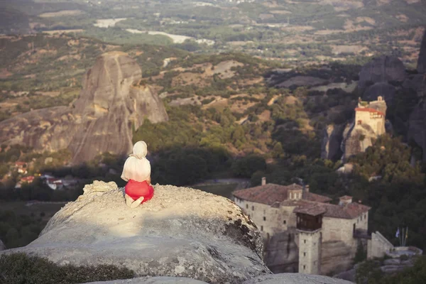 Menina sozinha em um vestido vermelho e cachecol na borda da rocha e reza nos mosteiros de Meteora. Feminino na rocha e mosteiros de Meteora, na Grécia, na Tessália — Fotografia de Stock