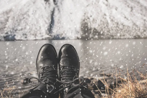 Female legs in black hiking boots against the background of snow mountains in Switzerland. Snow on women\'s shoes