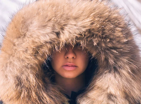 Beautiful girl in a hood with fur of a winter jacket. The girl\'s face is hidden in a hood with fur.
