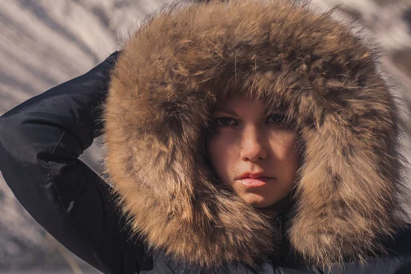 Schöne Mädchen in einer Kapuze mit Fell einer Winterjacke. Das Gesicht des Mädchens ist in einer Kapuze mit Fell versteckt. — Stockfoto