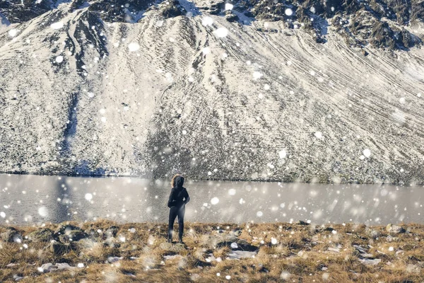 En flicka i en vinterjacka med päls ligger mittemot snö bergen och en sjö i Schweiz. Fluela passera i Schweiz i vinter. — Stockfoto