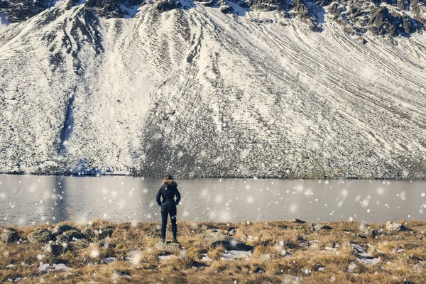 A girl in a winter jacket with fur stands opposite the snow mountains and a lake in Switzerland.  Fluela pass in Switzerland in winter. — Stock Photo, Image