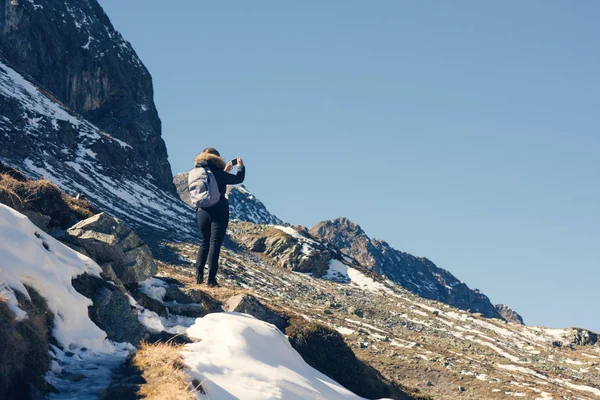 Uma fotógrafa com câmera e mochila em uma jaqueta de inverno com pêlo na montanha de neve na Suíça. Fluela passa na Suíça no inverno . — Fotografia de Stock