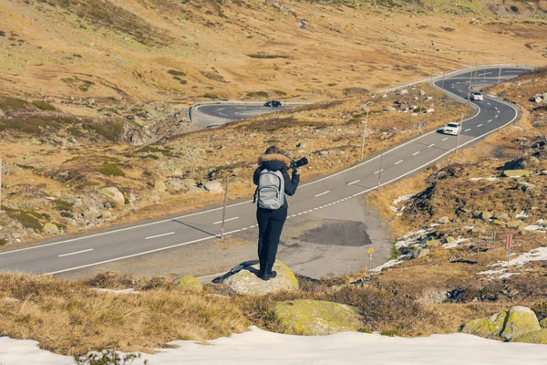 Uma fotógrafa com câmera e mochila em uma jaqueta de inverno com pêlo na montanha de neve na Suíça. Fluela passa na Suíça no inverno . — Fotografia de Stock