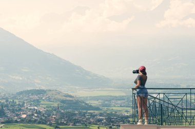 Bir kamera ile bir kırmızı şapkalı bir kız fotoğrafçı İtalyan dağlar ve Güney Tirol köyde balkonunda duruyor. Alto Adige