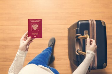 Pasaport kontrolü için havaalanında yürüyen bir bavul ve Rus pasaportu ile bir kızın üst görünümü.