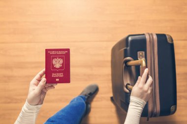 Pasaport kontrolü için havaalanında yürüyen bir bavul ve Rus pasaportu ile bir kızın üst görünümü.