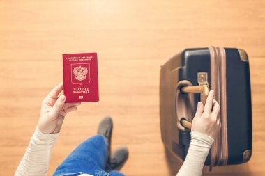 Pasaport kontrolü için havaalanında yürüyen bir bavul ve Rus pasaportu ile bir kızın üst görünümü.