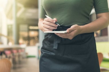 Önlüklü kadın garsonun kafedeki veya restorandaki not defteri ve kalemle sipariş vermeye hazır kesilmiş görüntüsü.. 