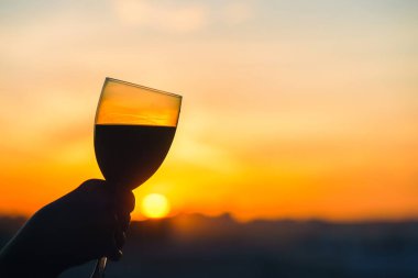 Gün batımında şarap kadehiyle kadın eli. 