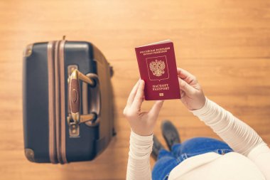 Pasaport kontrolü için havaalanında yürüyen bir bavul ve Rus pasaportu ile bir kızın üst görünümü.