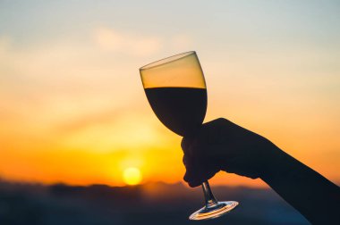 Gün batımında şarap kadehiyle kadın eli. 