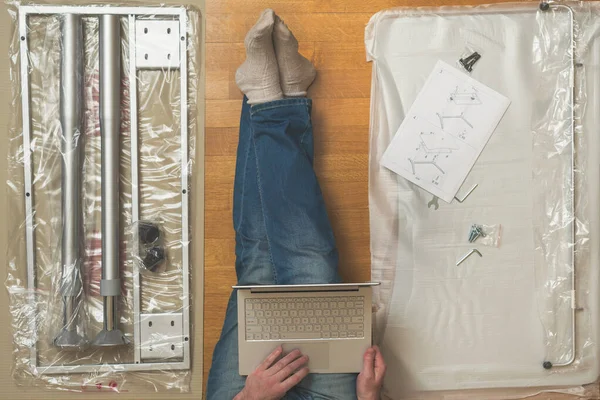 Man with laptop and furniture assembling Instruction. Top view