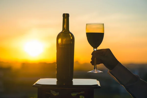 Silhouette of male and female hands toasting wine on sunset background. Romantic couple celebrating at a restaurant