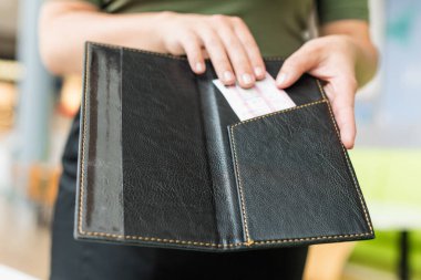 Önlüklü kadın garsonun kesilmiş görüntüsü kafe ya da restoran ziyaretçisine fatura klasörünü uzat.