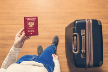 Pasaport kontrolü için havaalanında yürüyen bir bavul ve Rus pasaportu ile bir kızın üst görünümü.