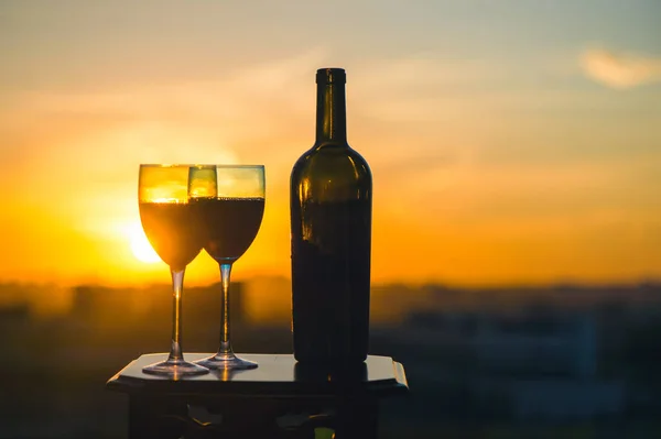 A bottle of wine and two glasses on a sunset background