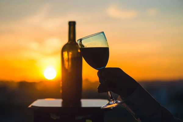 female hand with wine glass on sunset background.