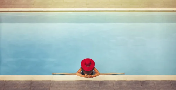 young female in a hat sits on a twine in the pool at sunset