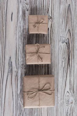 El işi kağıdına sarılı üç hediye kutusu ve kırsal ahşap, kahverengi, beyaz ve gri tahtalar üzerinde fiyonk halatı. Diy.