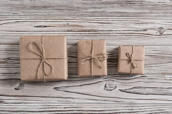 Three gift boxes packing in craft paper and bow rope on rustic wood brown, white and gray burned planks. DIY