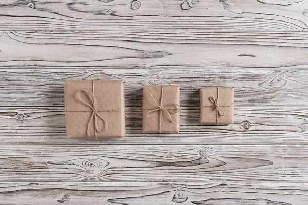 Three gift boxes packing in craft paper and bow rope on rustic wood brown, white and gray burned planks. DIY