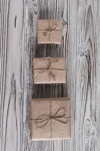 三个礼品盒 包装在工艺用纸和弓绳上的乡村木褐色 白色和灰色烧焦的木板 — 图库照片